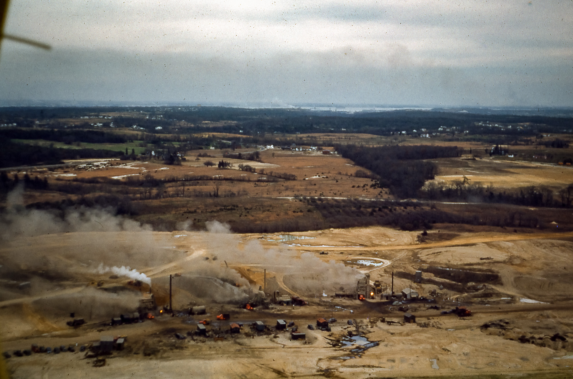 An aerial view of the construction of an airport with smoke rising from the ground as workers clear land.
