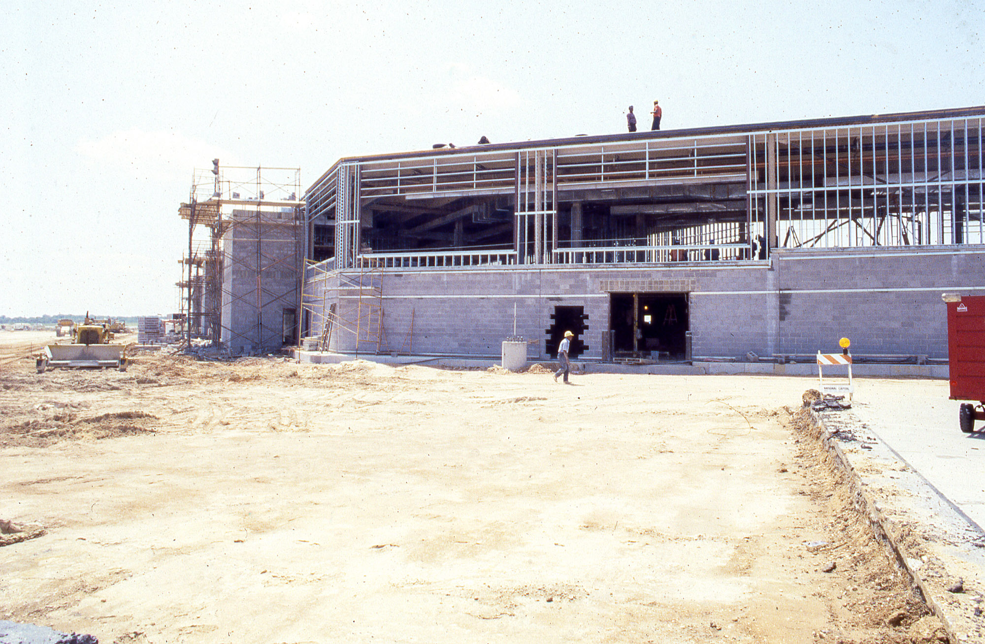 A cement and steel frame rises from the ground as workers walk near the construction site.