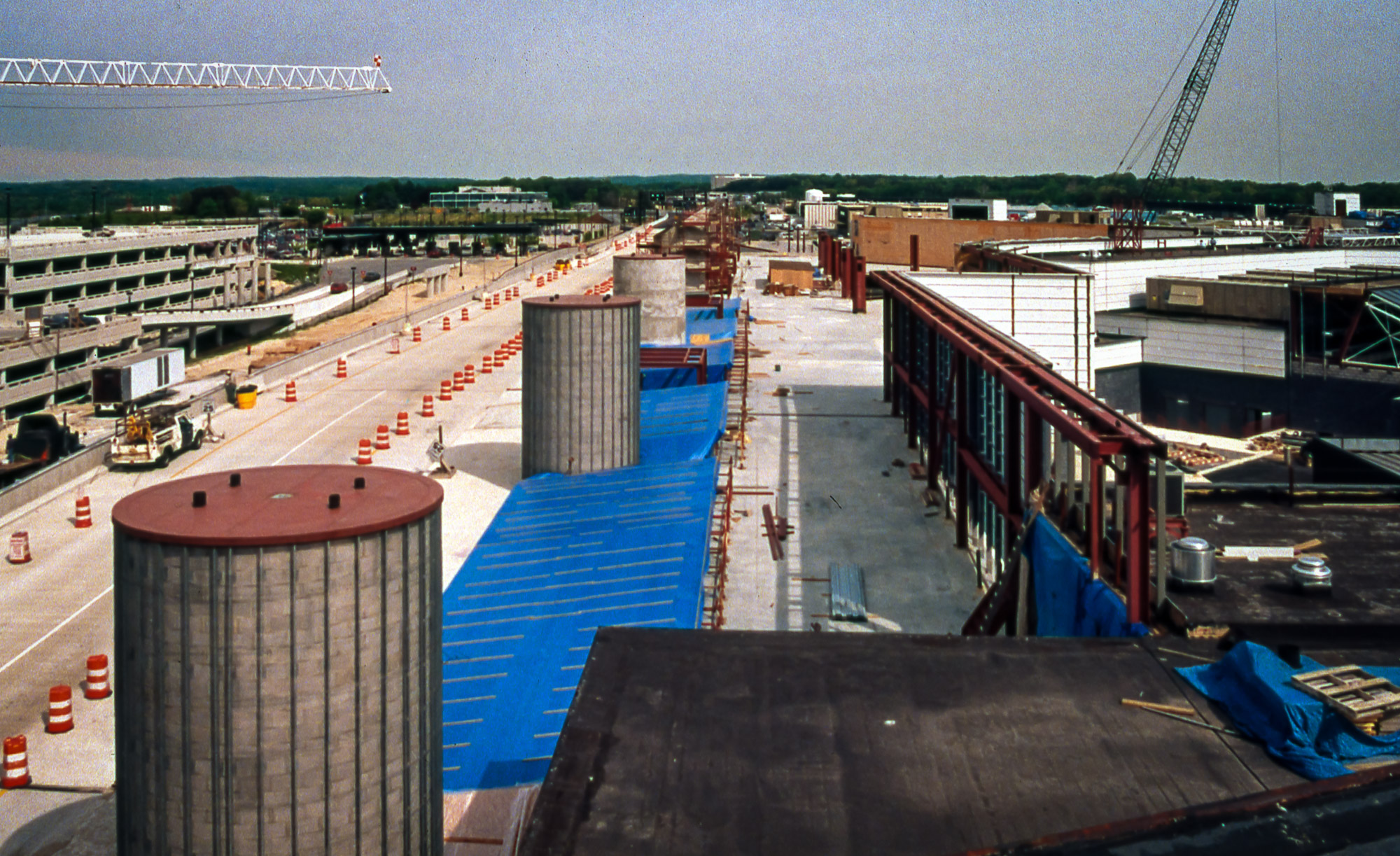 Cylindrical towers rise from the ground near a road, with orange construction cones lining the road.