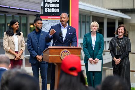 Phot of Governor Moore speaking behind a podium and standing around him is Lt. Governor Aruna Miller, Baltimore City Mayor Brandon Scott, Maryland Transportation Secretary Katie Thomson and MTA Administrator Holly Arnold.