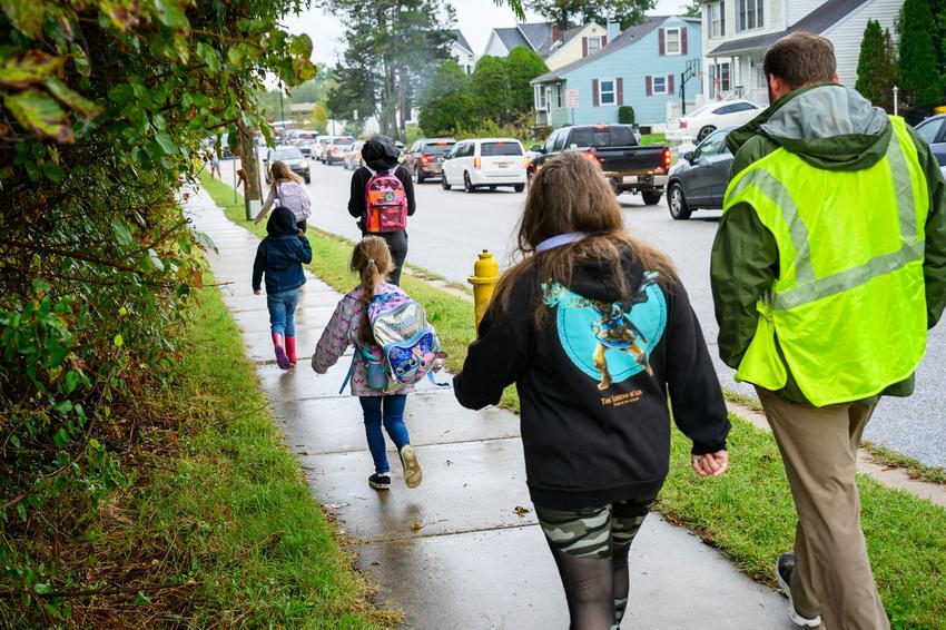 Students with backpacks walking on a sidewalk to school.