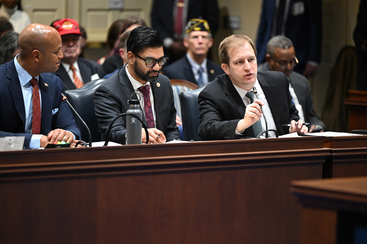 Three men sitting at a table during a legislative hearing.